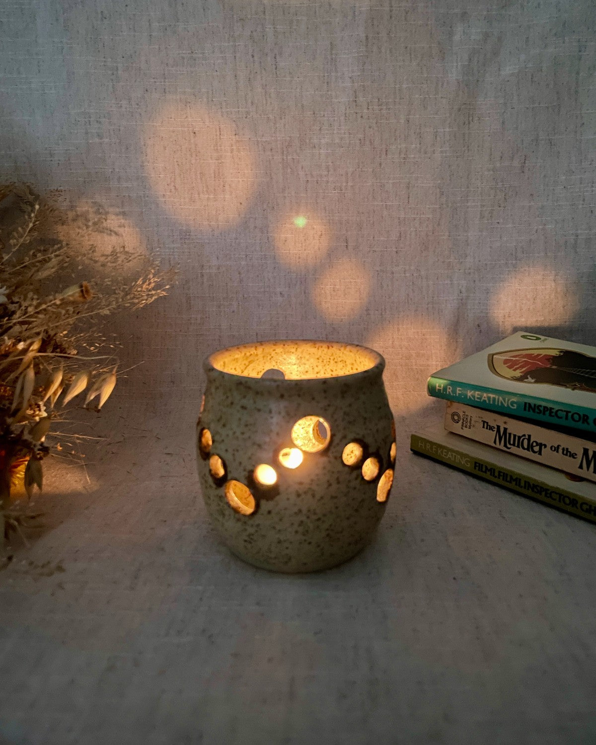 a stoneware tealight holder in the dark, with a candle lit inside showing the pattern the glow of the candle casts